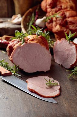 Eski ahşap bir masanın üzerinde tütsülenmiş jambon, baharat ve mutfak gereçleri. Seçici odak.