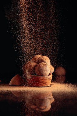 Kakao tozu serpiştirilmiş küçük ahşap tabakta çikolatalı trüf. Siyah yansıtıcı arka plan. Boşluğu kopyala.