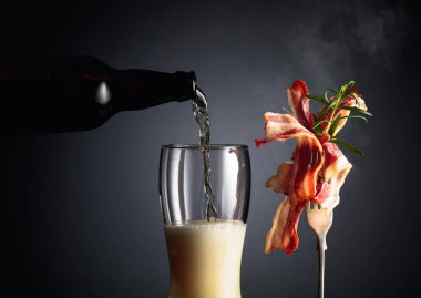 Bira ve biberiyeyle süslenmiş kızarmış domuz pastırması. Bira şişeden bardağa dökülür. Boşluğu kopyala.