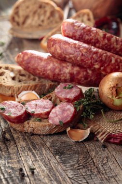 Dry-cured sausages with herbs and spices. Sausages with bread, thyme, pepper, onion, and garlic on an old wooden table. Simple healthy food. clipart