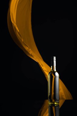 Siyah yansıtıcı arka planda bir şişe beyaz şarap. Sarı kumaş arka planda dalgalanıyor. Boşluğu kopyala.