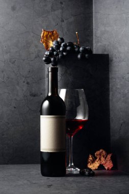 Siyah bir taş masanın üzerinde kurumuş asma yapraklı kırmızı şarap ve mavi üzümler. Eski boş bir şişede. 