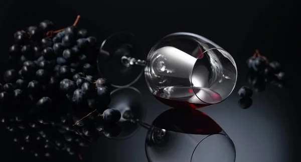 黒の反射的な背景に赤ワインとブルーブドウとワイングラス スペースのコピー — ストック写真