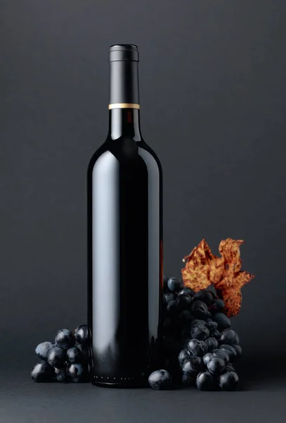 Butelka Czerwonego Wina Niebieskie Winogrona Wysuszonymi Liśćmi Winorośli Ciemnym Tle — Zdjęcie stockowe