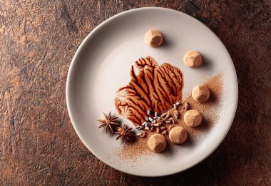 Bej bir tabakta çikolata soslu çikolatalı trüf mantarı. Tatlılar kakao tozu, çikolata parçacıkları ve anason ile süslenir. Yukarıdan görüntüle.