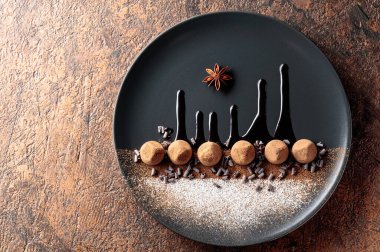 Çikolatalı trüf mantarı, siyah tabakta, çikolata soslu. Tatlılar kakao tozu ve pudra şekerle serpiştirilir. Üst görünüm. 