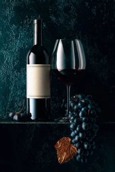 红葡萄酒和蓝色葡萄 葡萄干了 藤叶在旧的深蓝色背景上 在一个空的瓶子标签上 — 图库照片