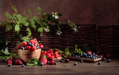 Bahçedeki eski ahşap bir masada çilek, yabanmersini, ahududu ve tatlı kiraz karışımının yakın plan renkli meyveleri. Yapraklı çeşitli meyveler.