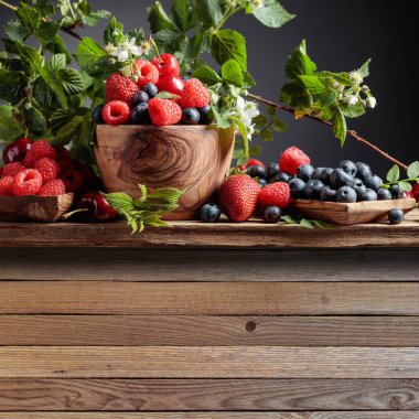 Çilek, yaban mersini, ahududu ve kiraz karışımı renkli meyveler eski ahşap bir masada. Yapraklı çeşitli meyveler. Metnin için boşluk kopyala.