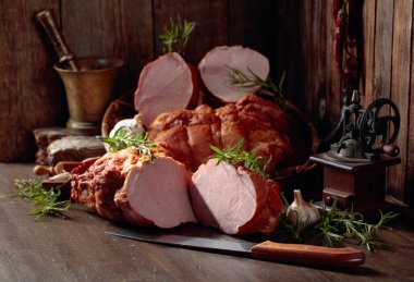 Eski ahşap bir masada tütsülenmiş jambon, baharat ve mutfak gereçleri..