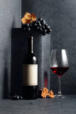Siyah bir taş masanın üzerinde kurumuş asma yapraklı kırmızı şarap ve mavi üzümler. Eski boş bir şişede. Boşluğu kopyala.