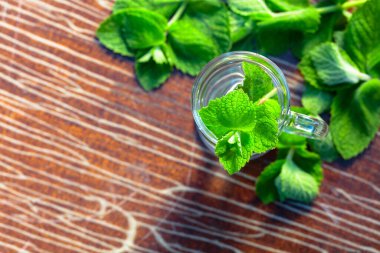 Bahçedeki eski ahşap bir masada nane çayı. Taze yeşil dallar ve sıcak çayla birlikte bardak. Üst görünüm, alanı kopyala.