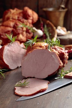 Eski ahşap bir masanın üzerinde tütsülenmiş jambon, baharat ve mutfak gereçleri. Seçici odak.