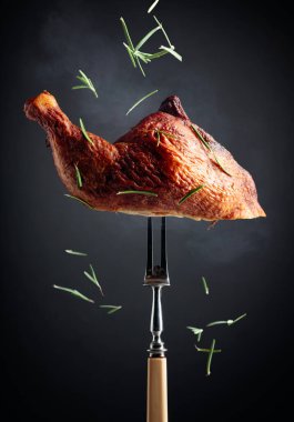 Smoked chicken thigh on a fork sprinkled with rosemary. Hot chicken on a black background. clipart