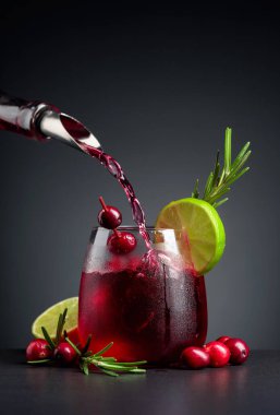 Böğürtlen, limon ve biberiyeyle süslenmiş yabanmersini kokteyli. Buzlu dondurulmuş bardakta kızılcık likörü dökülüyor. Boşluğu kopyala.