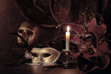 Karnaval maskeleri ve yanan mumlu küçük pirinç şamdanlar. Eski ahşap bir masada karnaval aksesuarları..