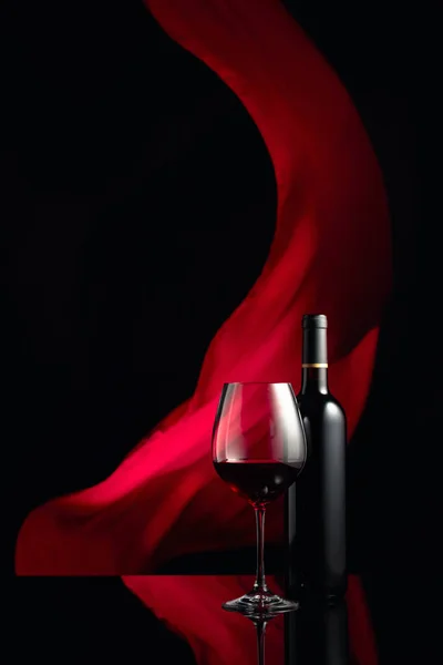 在黑色的反光背景上 盛满了红酒的瓶子和酒杯 红布在后面飘扬 复制空间 — 图库照片