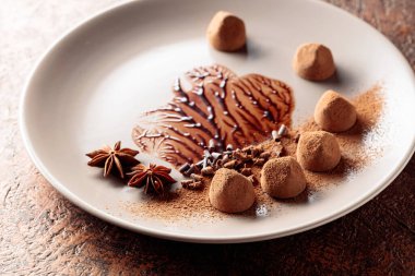 Bej bir tabakta çikolata soslu çikolatalı trüf mantarı. Şekerler kakao tozu, çikolata parçacıkları ve anason ile süslenir..