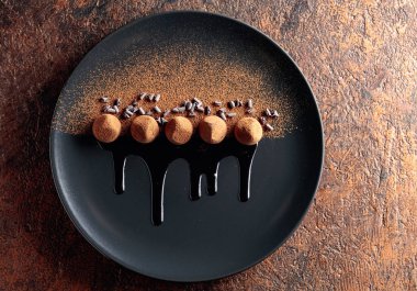 Çikolatalı trüf mantarı, siyah tabakta, çikolata soslu. Tatlılar kakao tozu serpiştirilir. Üst görünüm. 