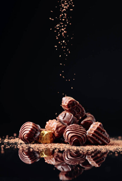 Различные шоколадные конфеты на черном фоне, посыпанные шоколадной стружкой. Копирование пространства.