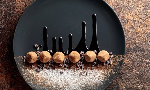 チョコレートソースをかけたブラックプレートにチョコレートトリュフ お菓子にはココアパウダーと粉砂糖を振りかける トップ表示 — ストック写真