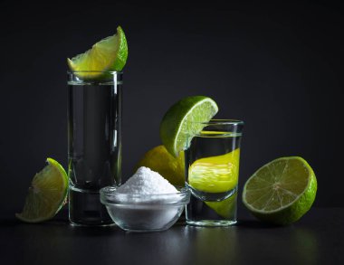 Siyah arkaplanda tuz ve limon dilimleri olan tekila..