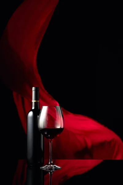 黒の反射的な背景に赤ワインのボトルとガラス 背景の赤い布のフラッター スペースのコピー — ストック写真