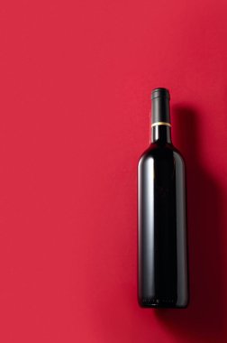 Kırmızı arka planda açılmamış bir şişe kırmızı şarap. Boşluğu kopyala.