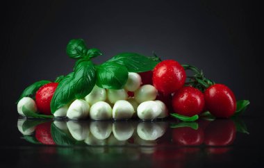 Yeşil fesleğenli Mozzarella ve siyah masadaki domatesler.