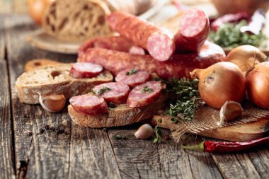 Kurutulmuş sosis ve baharatlı otlar. Ekmek, kekik, biber, soğan ve sarımsaklı sosisler eski ahşap bir masada. Basit sağlıklı yiyecekler..