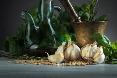 Ahşap bir masada pesto sosu yapmak için gerekli malzemeler. Pirinç havan, zeytinyağı, sarımsak, yeşil fesleğen, biberiye ve çam fıstığı..