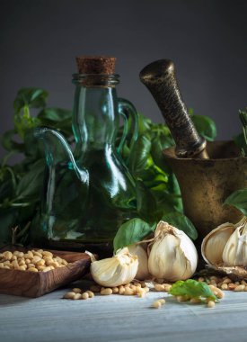 Ahşap bir masada pesto sosu yapmak için gerekli malzemeler. Pirinç havan, zeytinyağı, sarımsak, yeşil fesleğen, biberiye ve çam fıstığı..