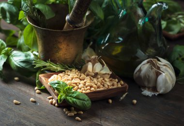 Ahşap bir masada pesto sosu yapmak için gerekli malzemeler. Pirinç havan, zeytinyağı, sarımsak, yeşil fesleğen, biberiye ve çam fıstığı..