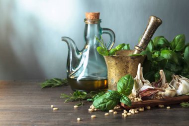 Ahşap bir masada pesto sosu yapmak için gerekli malzemeler. Pirinç havan, zeytinyağı, sarımsak, yeşil fesleğen, biberiye ve çam fıstığı..