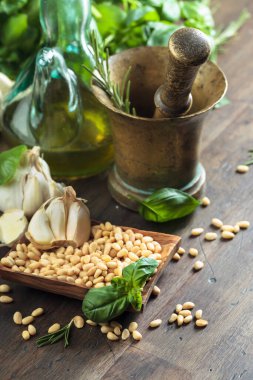 Ahşap bir masada pesto sosu yapmak için gerekli malzemeler. Pirinç havan, zeytinyağı, sarımsak, yeşil fesleğen, biberiye ve çam fıstığı..