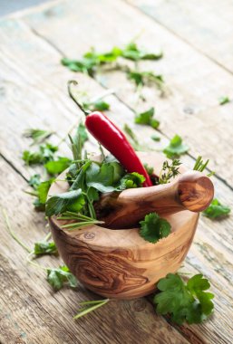 Eski ahşap bir masada biberli ahşap havan ve şifalı otlar. Havan, kırmızı biber, biberiye, kişniş, kekik ve maydanoz..