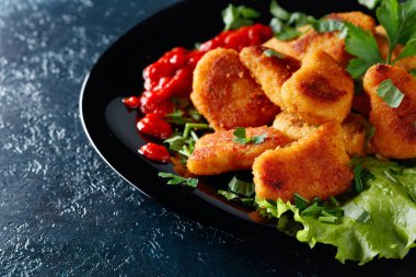  Ketçaplı kızarmış nugget, siyah tabakta doğranmış maydanoz serpiştirilmiş..