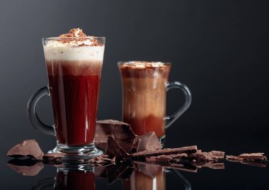 Krem şantili sıcak çikolata ve siyah yansıtıcı arka planda koyu çikolata parçaları. Boşluğu kopyala.