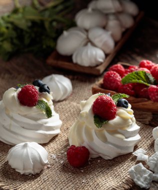 Pavlova 'ya ahududu, yaban mersini ve nane ekleyin. Pavlova tatlısı ve kırsal bir arka planda küçük kremalar.