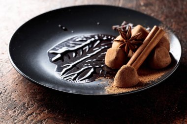 Çikolatalı trüf mantarı, siyah tabakta, çikolata soslu. Tatlılar kakao tozu serpiştirilir.. 