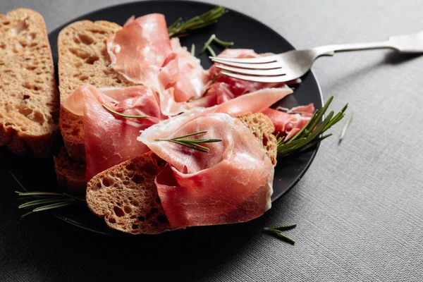 Prosciutto Met Brood Rozemarijn Een Zwarte Plaat — Stockfoto