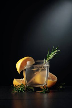 Buzlu, limonlu ve biberiyeli soğuk bir içecek. Siyah arka planda kokteyl cini ve tonik olan donmuş bardak. Boşluğu kopyala.