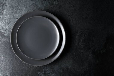 Siyah taş bir masanın üzerine boş siyah tabaklar. Üst görünüm, alanı kopyala.