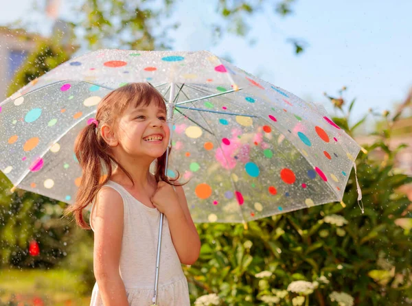 幸せな女の子は傘で夏の雨の下で庭で遊ぶ — ストック写真