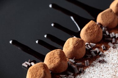 Çikolatalı trüf mantarı, siyah tabakta, çikolata soslu. Tatlılar kakao tozu ve pudra şekeriyle serpiştirilir..