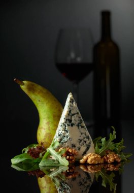 Cevizli, armutlu ve yeşillikli mavi peynir. Arka planda, bir kadeh kırmızı şarabın silüeti var..