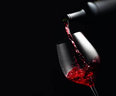 Bardağa kırmızı şarap dolduruyorum. Kopyalama alanı olan siyah arkaplan.