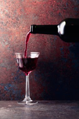 Porto şarabı veya güçlendirilmiş kırmızı şarap paslı kahverengi arka planda bir şişeden bir bardağa dökülür. Boşluğu kopyala.