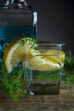 Mavi cin, tonik ve limonlu kokteyl. Limon dilimli alkol içeceği ve eski ahşap bir masada ardıç dalı..