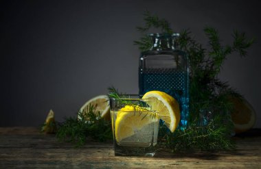 Mavi cin, tonik ve limonlu kokteyl. Limon dilimli alkol içeceği ve eski ahşap bir masada ardıç dalı..